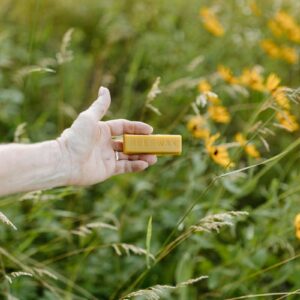 A hand holding a piece of yellow paper in a field of yellow flowers